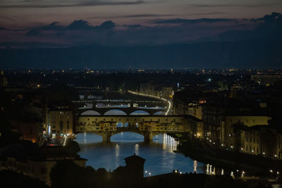 High angle view of illuminated bridge over river by buildings in city at night