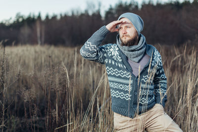 Young man looking away while standing on grassy field in forest