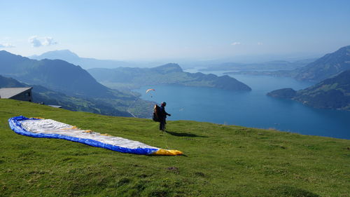 Person preparing for paragliding on mountain by sea against sky