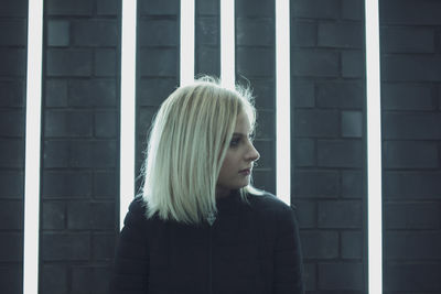 Close-up woman looking away while standing against illuminated lights on wall