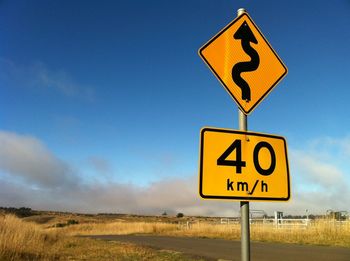 Information sign on road by field against sky