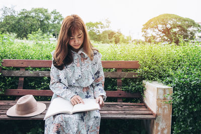 Young woman sitting on seat against trees