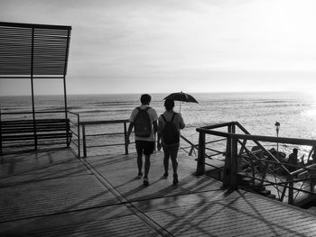 Rear view of people standing on beach against sky