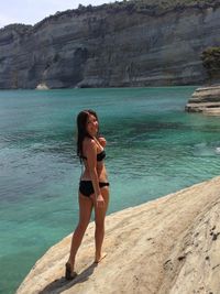 Full length portrait of sensuous woman in bikini on rock by sea