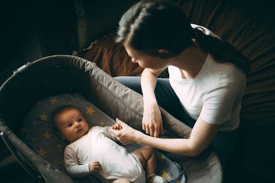 Mother looking at toddler boy resting in cot at home