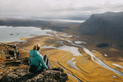 Rear view of man sitting on mountain against sky