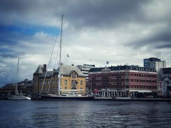 Buildings by river against cloudy sky