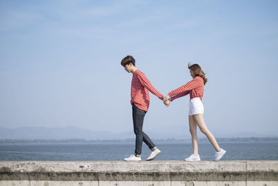 Couple walking together on retaining wall against sea