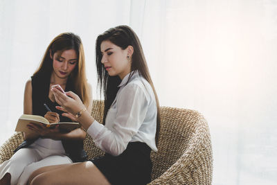 Businesswomen discussing while sitting on seat in office