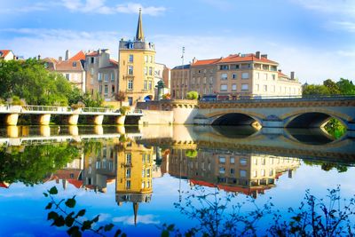 Arch bridge over river by buildings against sky