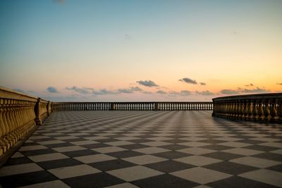 Footpath by railing against sky during sunset