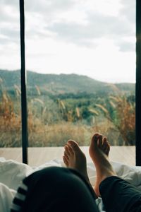 Low section of man relaxing bed against window