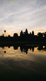 Silhouette built structures against calm lake at sunset