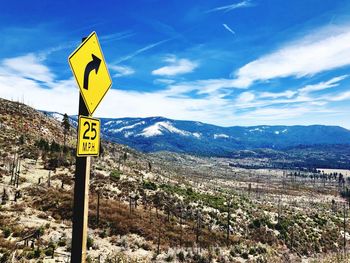 Road sign on mountain against sky