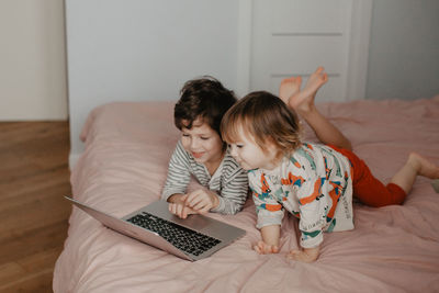 Little brother and sister lie in the bedroom on the bed and look at the laptop. high quality photo