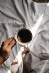 Cropped image of woman holding coffee cup on bed