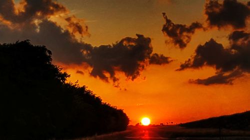 Silhouette trees against dramatic sky during sunset