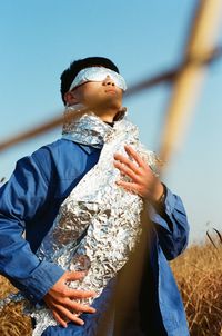 Low angle view of man with aluminum foil standing on field against sky