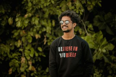 Young man standing against trees