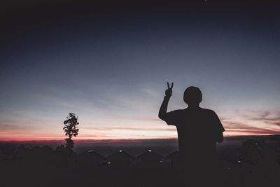 Silhouette man gesturing peace sign against sky during sunset