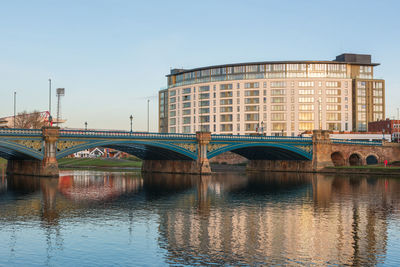 Bridge over river by buildings against clear sky