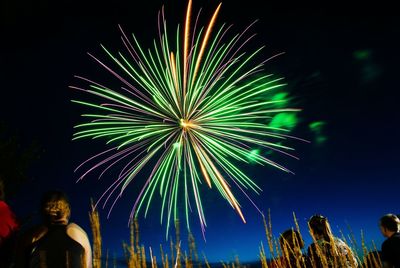 Low angle view of people looking at firework display at night