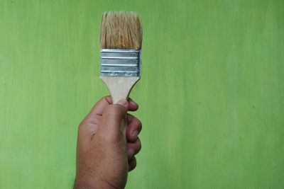 Close-up of hand holding paintbrush against green wall