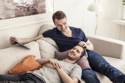 Young gay man holding digital tablet while partner sleeping on lap at home