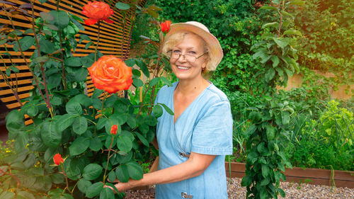 Portrait of smiling senior woman standing by plants