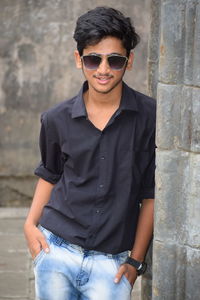 Portrait of young man wearing sunglasses standing by wall