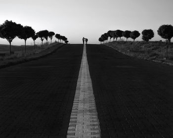 Empty footpath amidst trees against clear sky