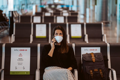 Woman wearing mask talking on phone while sitting at airport