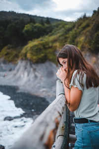 Side view of young woman standing against waterfall