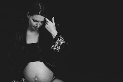 Pregnant woman sitting against black background