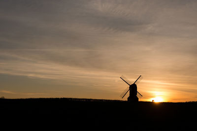 Silhouette traditional windmill on field against sky during sunset