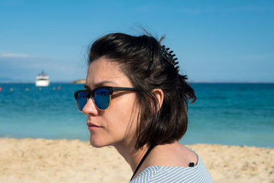Portrait of woman wearing sunglasses at beach against sky
