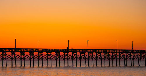 Silhouette pier over sea against orange sky