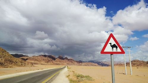 Road passing through desert against cloudy sky