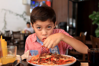 Portrait of boy eating food at table in restaurant