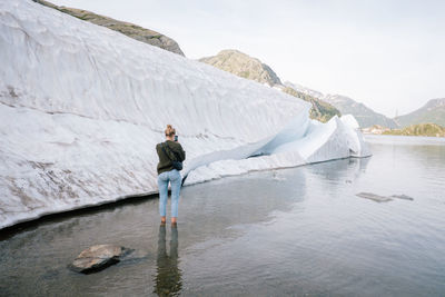 Woman photographing iceberg on frozen lake