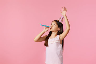 Young woman with arms raised standing against pink background
