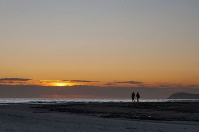 Silhouette people standing on beach against sky during sunset