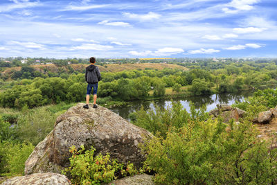 Rear view of boy standing on rock against sky