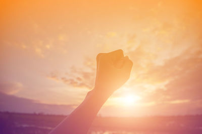 Cropped hands of woman clenching fist against cloudy sky during sunset