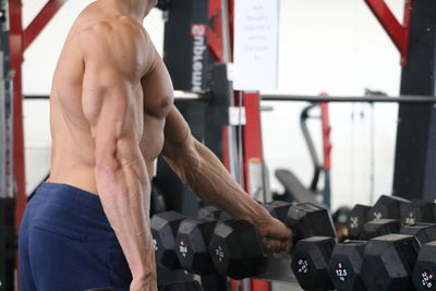 Midsection of shirtless man holding dumbbell in gym