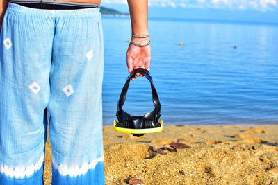 Midsection of man holding scuba mask at beach 