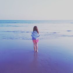 Rear view of girl standing on beach against sky