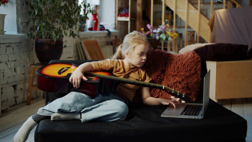 Girl holding guitar while looking at laptop