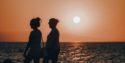 Silhouette friends standing by sea against sky during sunset