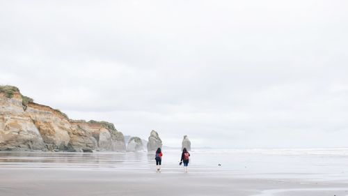 Rear view of men on beach against sky